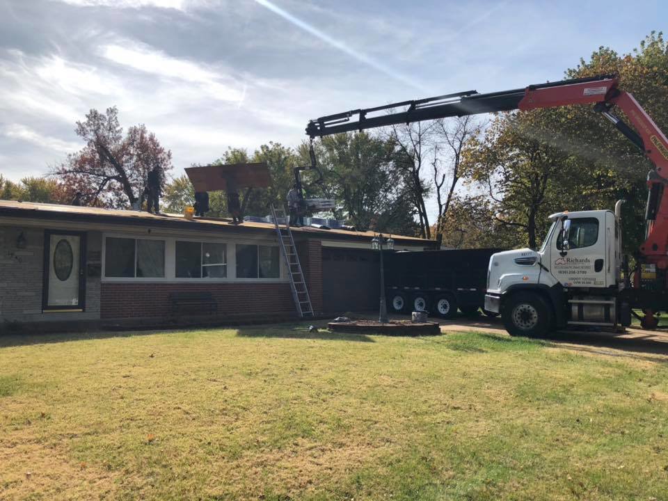 A roofing crew using a crane to lift materials during a roof installation by Gwen Co in St. Louis, MO.