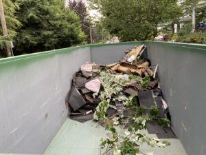 A large dumpster filled with old roofing shingles and construction debris from a project by Glick's Exteriors in Philadelphia, PA.
