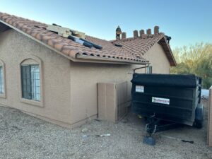 A dumpster trailer from Southwestern Dumpster Rental and Junk Removal parked next to a house during a roofing project, used for debris removal in Peoria, AZ.