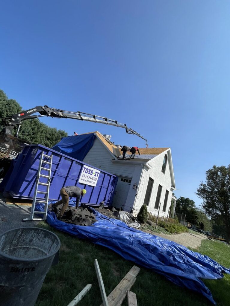 Workers removing roofing debris and loading it into a Toss-It dumpster during a construction project in Baltimore, MD.