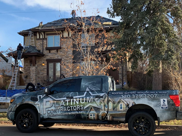Workers performing roofing installation or repair on a house, with a Platinum Contractors LLC truck in Greenwood Village, CO.