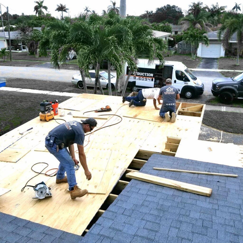 Construction workers installing plywood decking and shingles on a roof, demonstrating a general contractor project by JNY Remodeling INC in Fort Lauderdale, FL.
