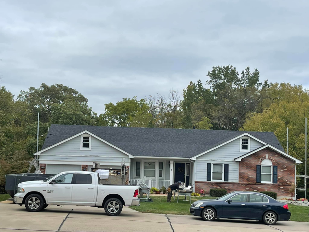 A house undergoing a roofing job with a dumpster and truck, provided by Remodeling by Simplified Solutions in Saint Charles, MO