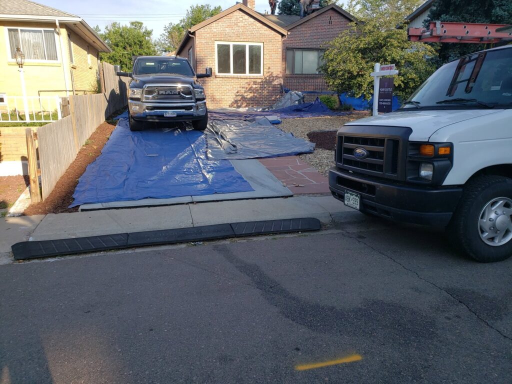Preparation for a roofing project with protective tarps and work vehicles at a home by Jesse Roofs Co. in Denver, CO