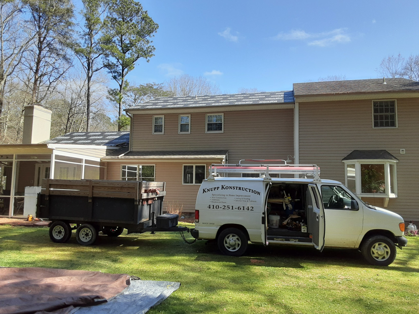 A Knupp Konstruction van and trailer parked at a home with a roofing project in progress in Salisbury, MD.