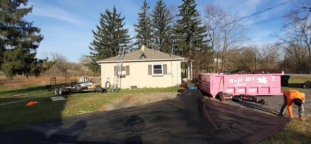 A residential roofing project with a dumpster and protective tarps by Manny's Sb Construction Inc in Goshen, NY.