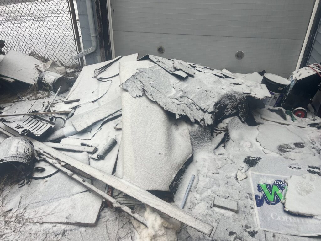 A pile of roofing shingles and construction debris covered in snow, requiring removal by Feelin Good Junk Removal & Estate Sales at 1111 Debra Lane.