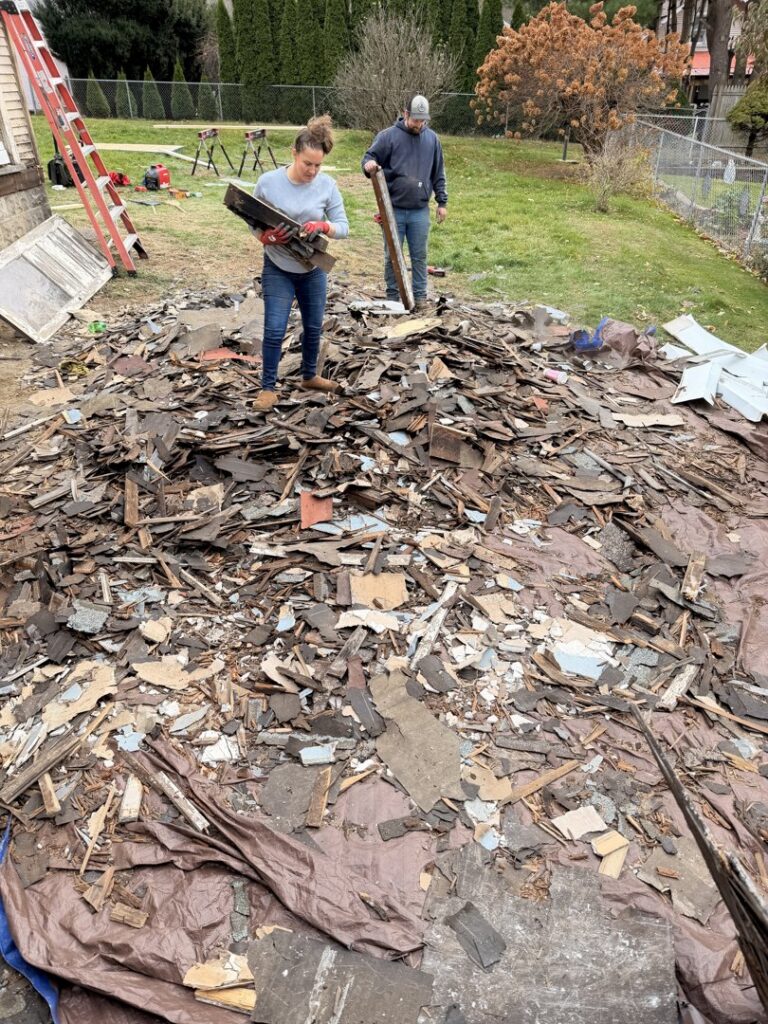 Two workers from Just Junk It standing on a large pile of roofing shingles and debris, ready for removal in Lancaster, PA.
