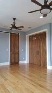 Interior room featuring light blue walls, rustic barn doors, and ceiling fans by Charter Bay Home Builders in Tampa, FL