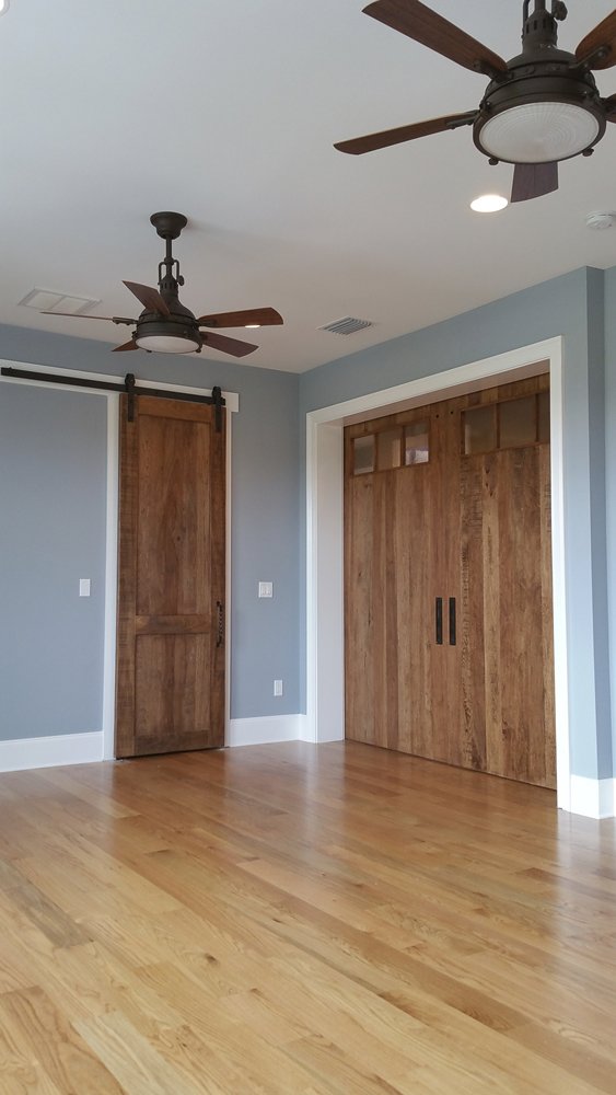 Interior room featuring light blue walls, rustic barn doors, and ceiling fans by Charter Bay Home Builders in Tampa, FL