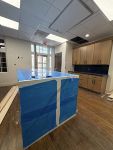 Room featuring installed cabinets, countertop, and a large island wrapped in protective film by Capitol Construction and Roofing LLC in Raleigh, NC