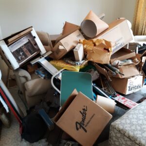 A room heavily cluttered with boxes, furniture, and various items, showcasing a large-scale junk removal project for Trash Monkey Junk Removal in Charleston, WV.