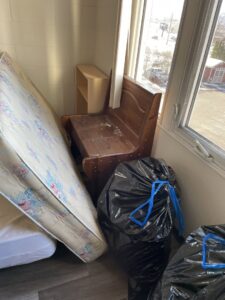 A room corner with old mattresses, a wooden bench, and black trash bags ready for junk removal by Missoula Junk Removal, LLC in Missoula, MT.