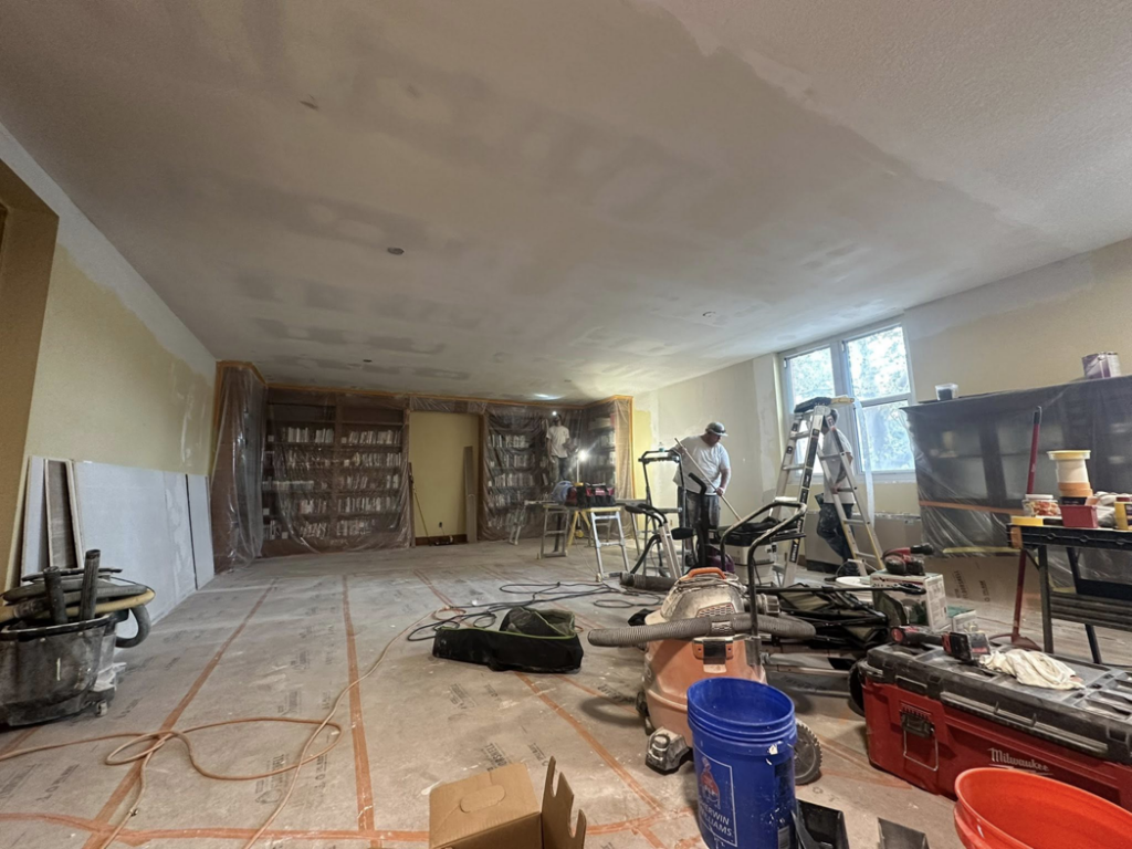 A large room undergoing drywall installation and renovation with workers and tools by ThoroughFair Renovations in Lawrence, KS.