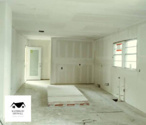 A room with newly installed drywall and a stack of drywall sheets, ready for finishing by Waterbury Drywall in Waterbury, CT.
