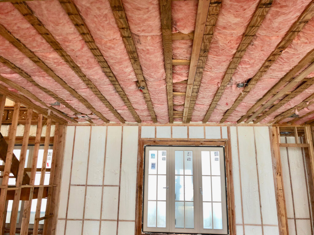 An unfinished room with fiberglass insulation in the ceiling and spray foam insulation on the walls by Spray Foam Art-Insulation in Stamford, CT.