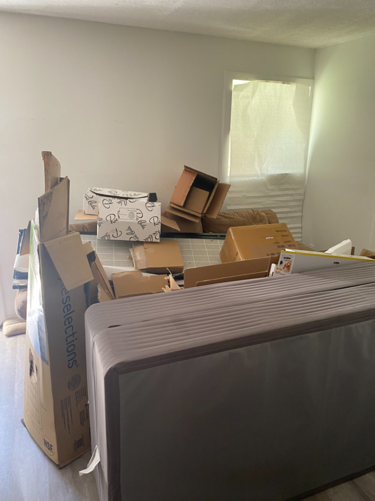A room cluttered with cardboard boxes, a mattress foundation, and debris, awaiting junk removal by Total Junk and Bulk Disposal in Whitsett, NC