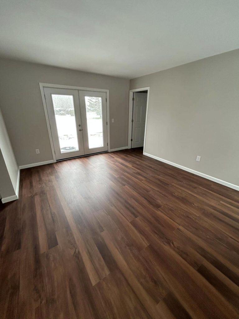 A renovated room featuring new hardwood flooring and modern French doors installed by Rock Solid Construction in Rochester, NY
