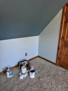 A room painting project with an angled ceiling and walls, showing paint cans on the carpet, by Sanders Construction & Handyman Services, LLC in Oklahoma City, OK.