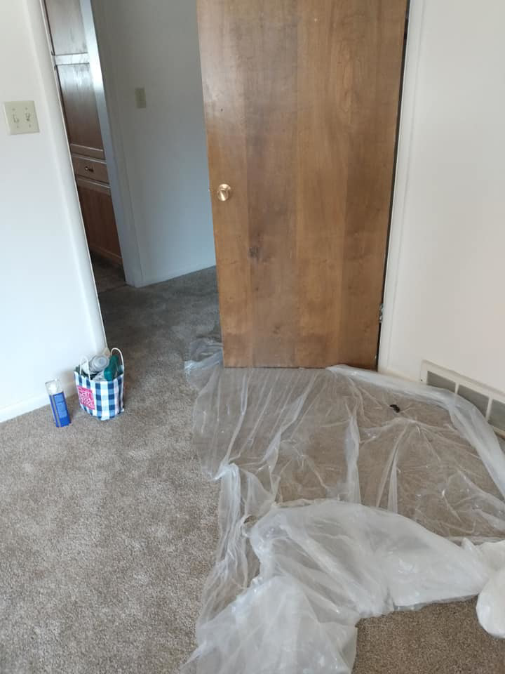 A room prepared for handyman services with plastic sheeting on the carpet and a wooden door propped up by Bevard Enterprises in Millcreek, UT.