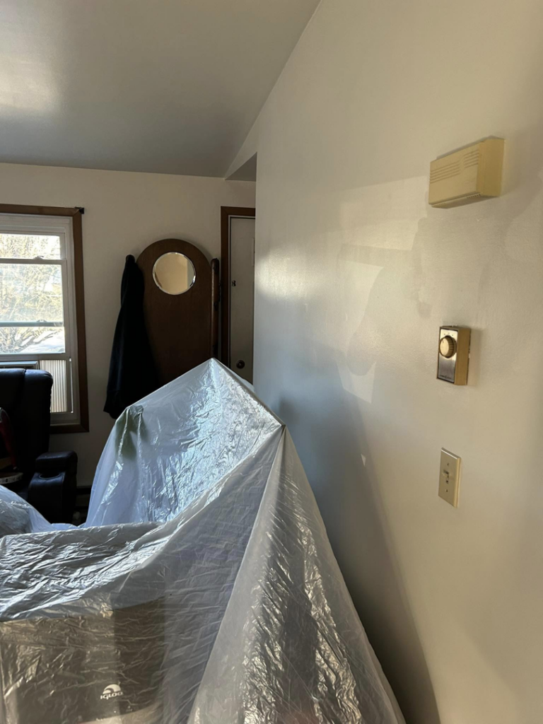 A living room with furniture covered in plastic sheeting, prepared for painting or repair work by Nick's Handyman Services in Martinsburg, WV.