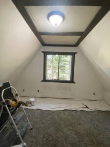 A room with sloped ceilings prepped for painting or renovation, with tools and drop cloths, by The Handy Nevadan LLC in Reno, NV.