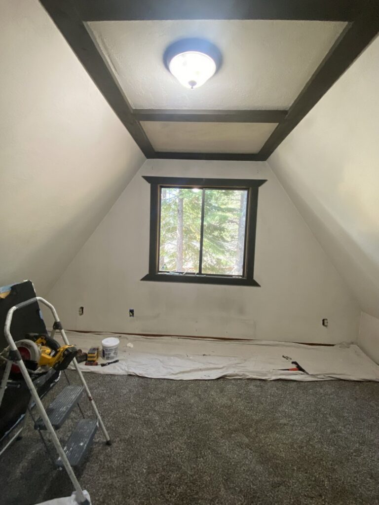 A room with sloped ceilings prepped for painting or renovation, with tools and drop cloths, by The Handy Nevadan LLC in Reno, NV.