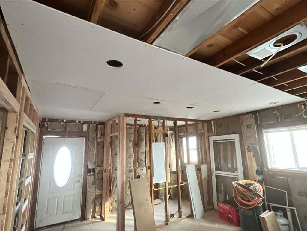A room under renovation showing partial drywall ceiling, exposed framing, and electrical wiring by Kliesen Construction Company in Pueblo, CO.