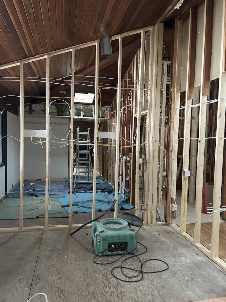 A room under renovation with exposed wall framing, electrical wiring, and a dehumidifier by Haus Builders in Goodhue, MN