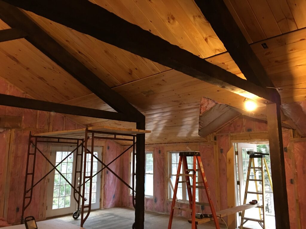 An interior room renovation in progress with exposed wood beams, insulation, scaffolding, and ladders by BizMick Construction in Coventry, RI.
