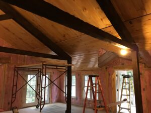 An interior room renovation in progress with exposed wood beams, insulation, scaffolding, and ladders by BizMick Construction in Coventry, RI.