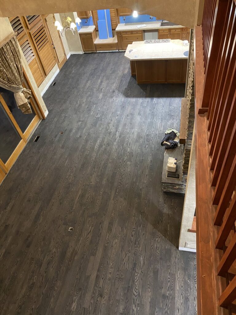 A large room under renovation with newly installed light hardwood floors and partially finished walls by IHS flooring LLC in Brighton, CO.