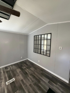 A newly updated room with dark laminate flooring, gray painted walls, a decorative mirror, and a ceiling fan installed by Hard Knox Handyman in Knoxville, TN.
