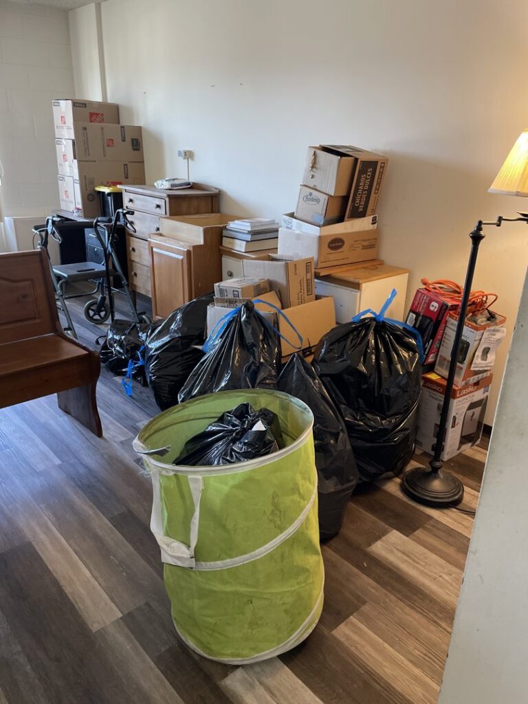 A room with stacks of moving boxes, furniture, and black trash bags, indicating a cleanout service by Missoula Junk Removal, LLC in Missoula, MT.