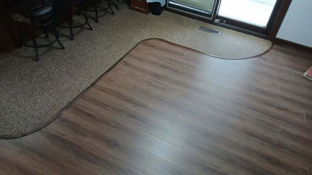 A room showcasing a professional installation of mixed wood-look laminate and carpet flooring with a smooth transition by Prime Construction And Flooring in Lorain, OH.