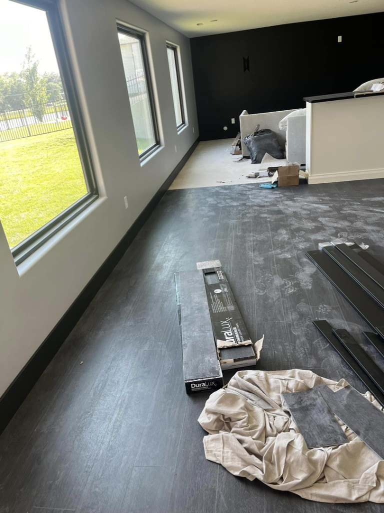A room with boxes of new DuraLux flooring planks, indicating a flooring installation project by Drew's Home Repair and Handyman Service in Wichita, KS.