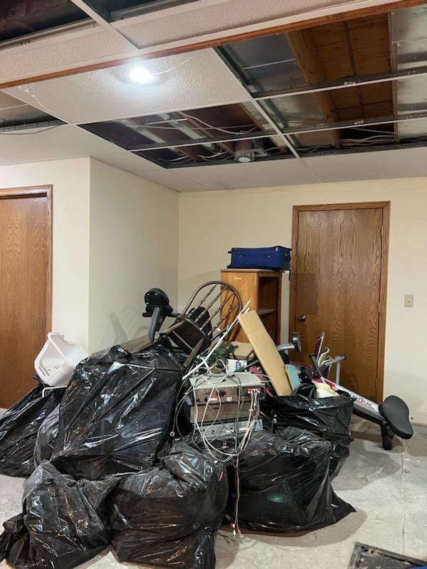 A room with large piles of black trash bags and various junk items, indicating a cleanout job by KJ Haul Away Junk Removal in Cedar Rapids, IA.