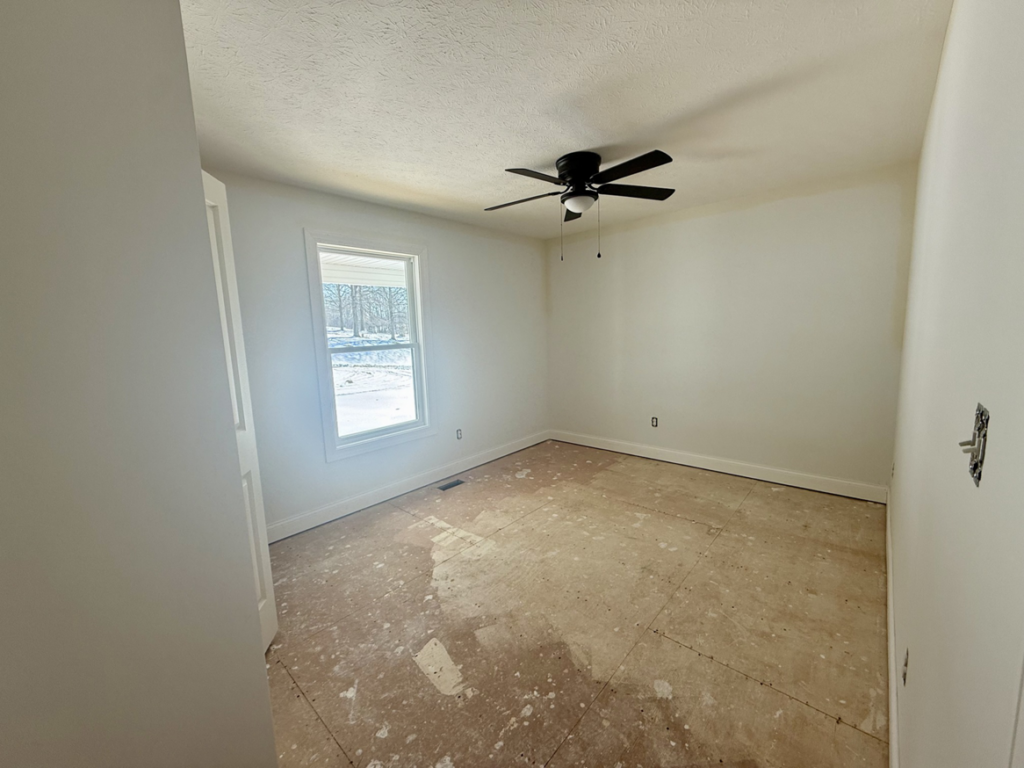 An empty room with subfloor exposed and a ceiling fan, ready for renovation by Phillips Homes, LLC in Elizabethtown, KY.