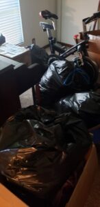 A room filled with black trash bags, boxes, and an exercise bike, indicating a cleanout service by Junk Fade Away, LLC in Jacksonville, FL.