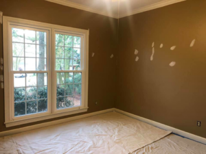 A room with brown walls showing wall repairs and spackle, with drop cloths on the floor, by Your Handy Helper in Mobile, AL