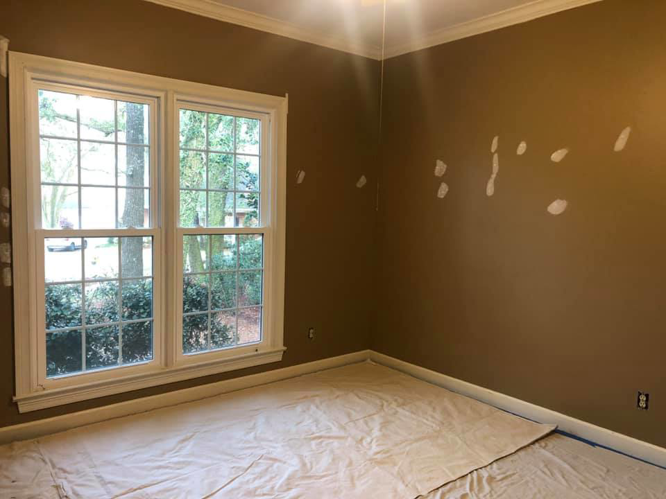 A room with brown walls showing wall repairs and spackle, with drop cloths on the floor, by Your Handy Helper in Mobile, AL