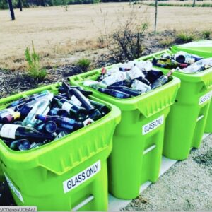 A row of three Fisher Recycling 'GLASS ONLY' bins filled with glass bottles in Charleston, SC.