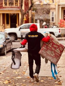 A Rubbish Doctor employee carrying junk on a sidewalk with a branded truck in the background in Portland, ME.