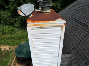 An aerial view of a residential chimney showing rusted metal flashing and white siding in need of repair by Hyde Roofing, LLC in Birmingham, AL