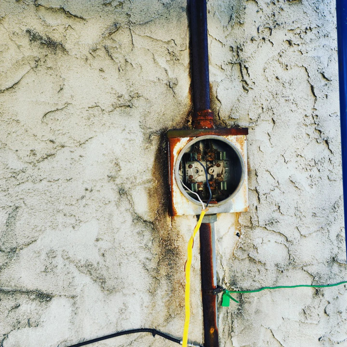 A rusted outdoor electrical box on a textured wall, indicating repair work by CJM Builders Inc in Wilmington, MA.
