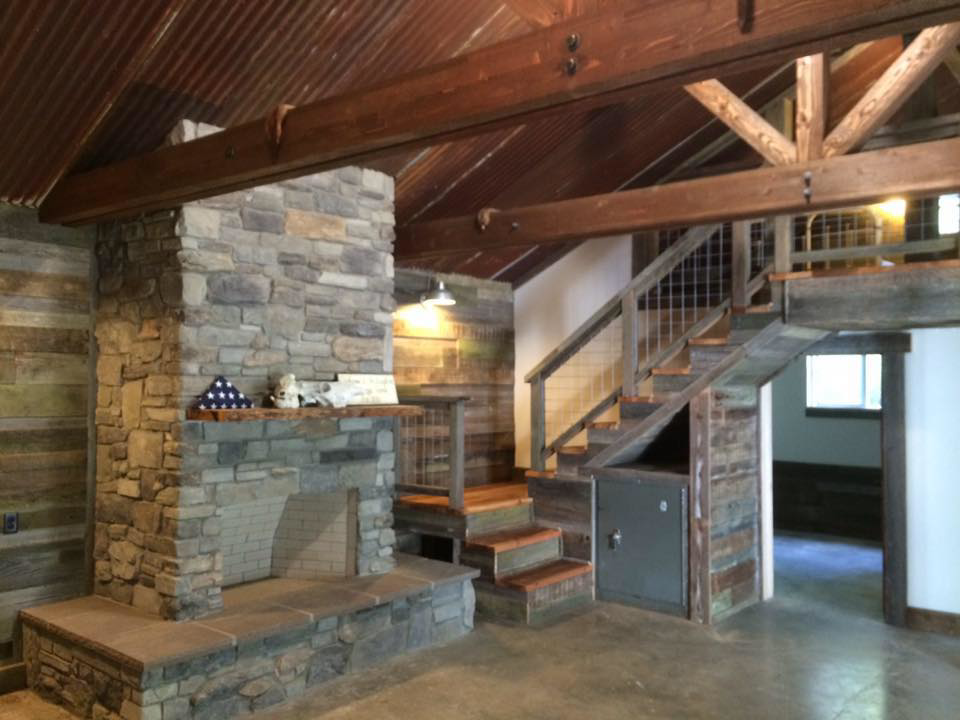 A rustic interior featuring a stone fireplace, exposed wood beams, and a custom staircase by R2S Build in Eugene, OR.