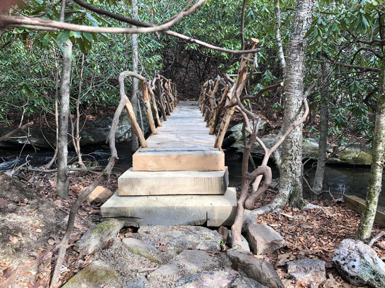 A newly constructed rustic wooden bridge with natural branch railings over a stream. Completed by Vasse Vaught Metalcrafting in Roanoke, VA.
