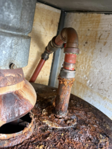 A close-up of a severely rusty pipe connection on an old water heater, showing a repair need by High Tide Home Remodeling in Charleston, SC.