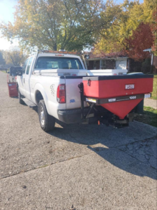 The rear of a white pickup truck with a red salt spreader attached, used by 24/7 Snow Removal & Salting for salting services in Indianapolis, IN.