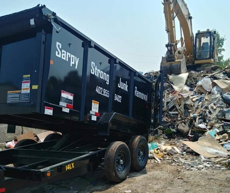 A Sarpy Strong Junk Removal trailer positioned at a large debris site with an excavator, showing services by Omaha Junk Removal in Papillion, NE